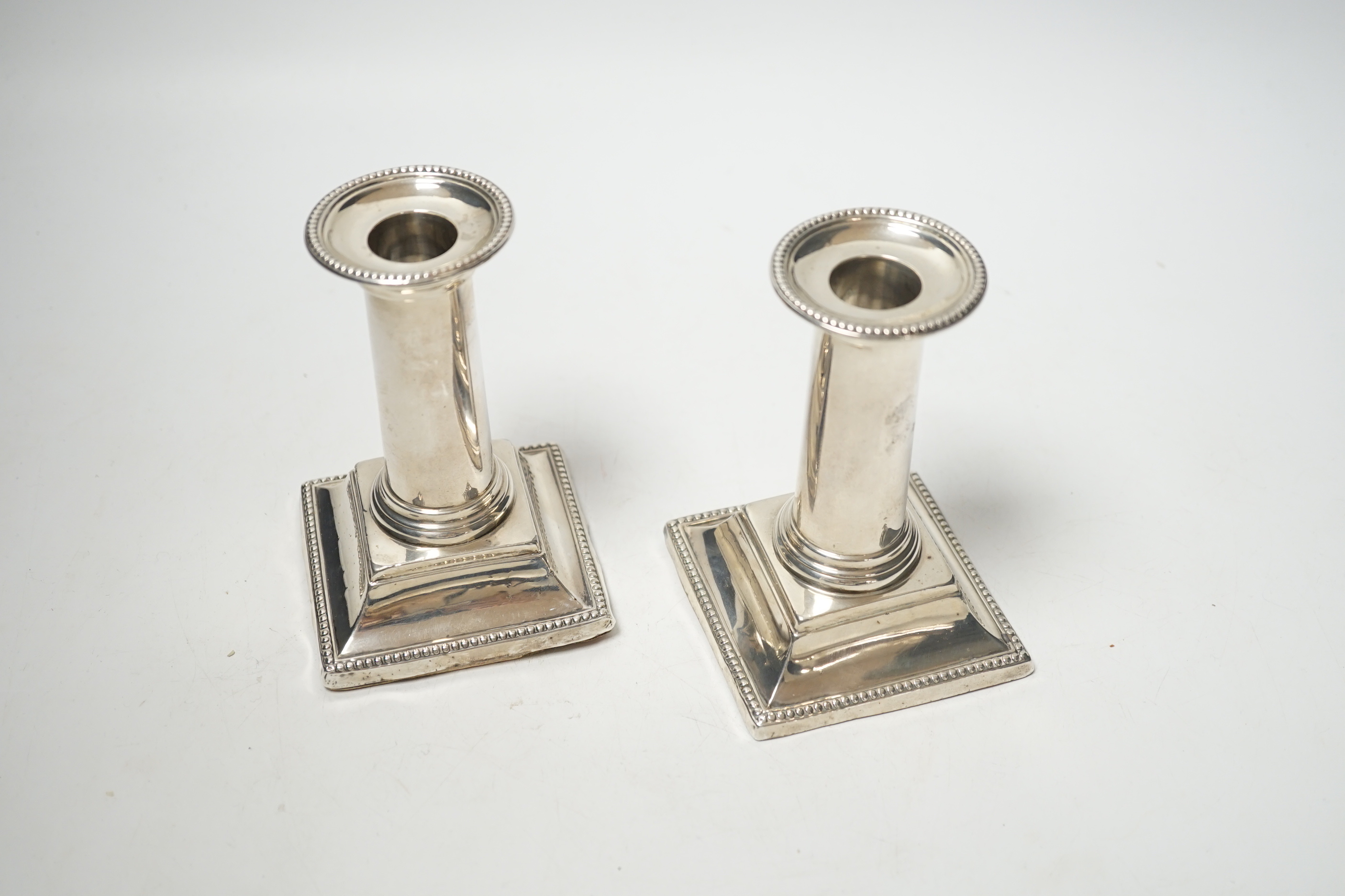 A pair of late Victorian silver dwarf candlesticks, with beaded borders, Edward Hutton, London, 1882, 11.7cm, weighted.